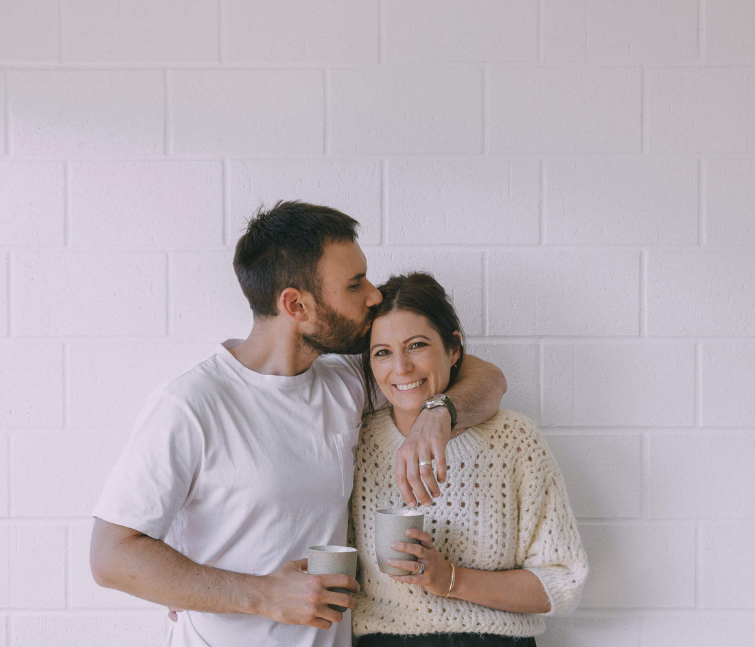 Perth coffee roaster and Coffee Beans Perth owners, Jess & Cal, standing against wall with a Perth coffee in hand.